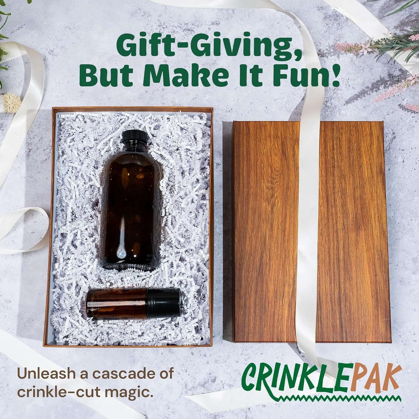 White crinkle paper shredded filler cushioning a brown glass bottle and a small roller bottle inside a wooden gift box with lid and decorative ribbon