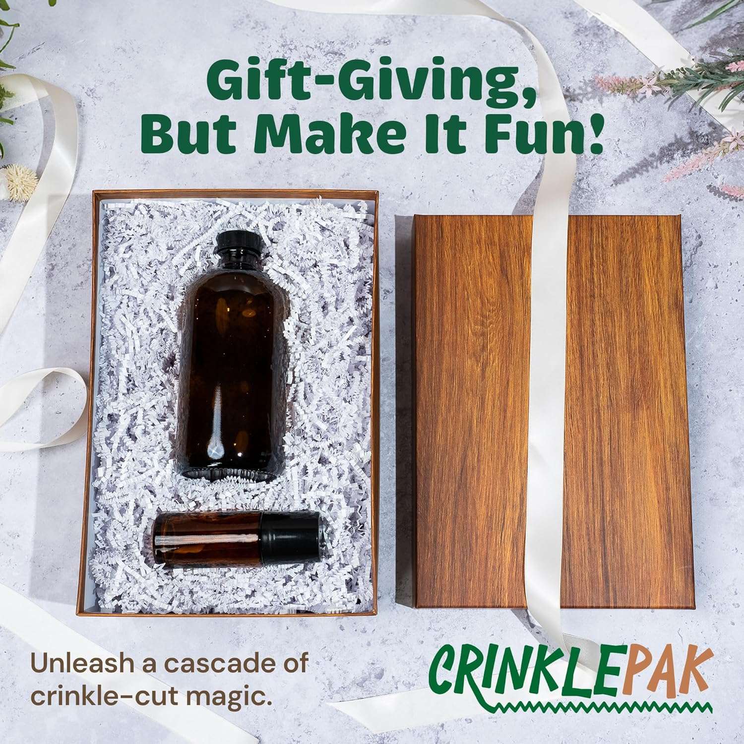 White crinkle paper shredded filler cushioning a brown glass bottle and a small roller bottle inside a wooden gift box with lid and decorative ribbon